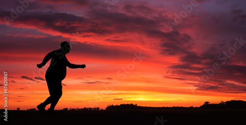 Silhouette of funny overweight man jogging at the sunset