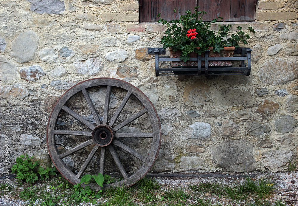 An old wooden wheel leaning against a stone wall