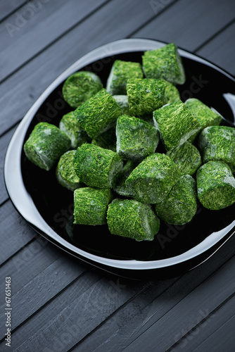 Glass plate with spinach cubes, black wooden background
