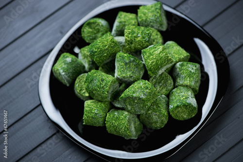 Spinach cubes in a glass plate, black wooden background