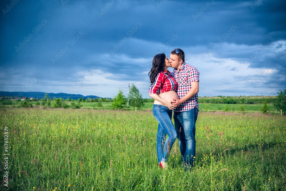 husband and his pregnant wife are walking at sunset in field on husband and his pregnant wife are walking at sunset in field on
