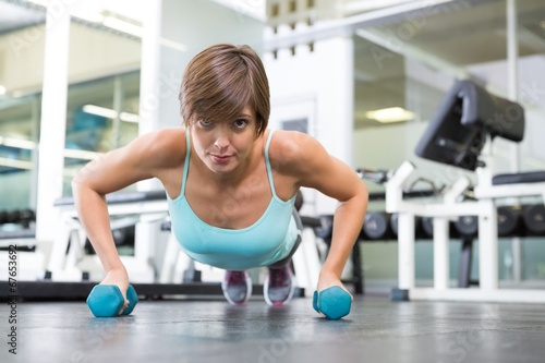 Fit brunette in plank position with dumbbells