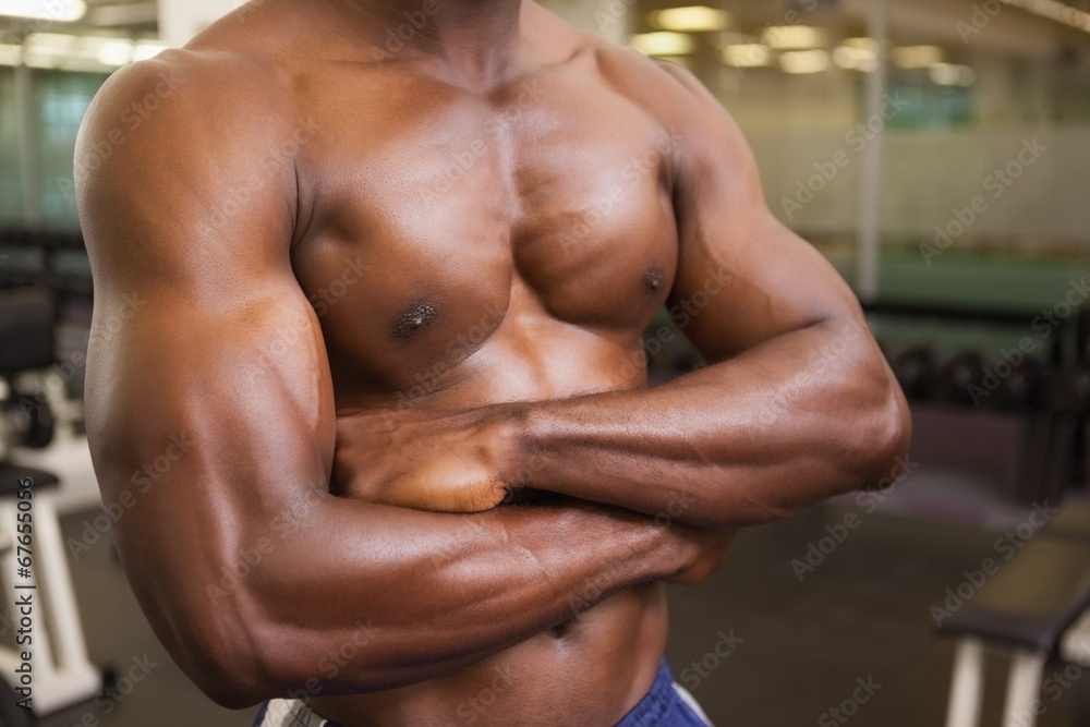 Shirtless muscular man with arms crossed in gym