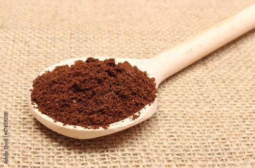 Ground coffee lying on wooden scoop. Jute background