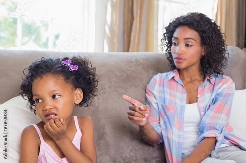 Pretty mother sitting on couch scolding petulant daughter