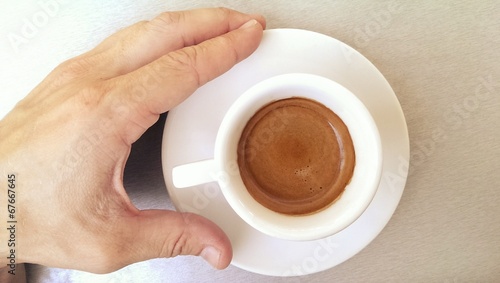 Small white cup of strong black espresso coffee and male hand