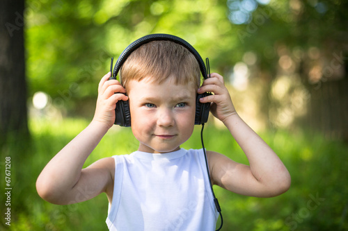Funny little boy with headphones outdoors.