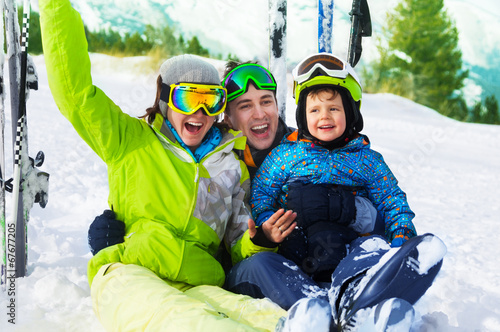 Happy parents and boy with ski masks sit on snow