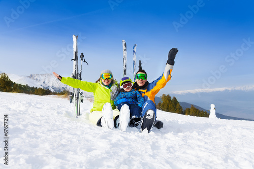 Excited parents and kid in ski masks sit on snow