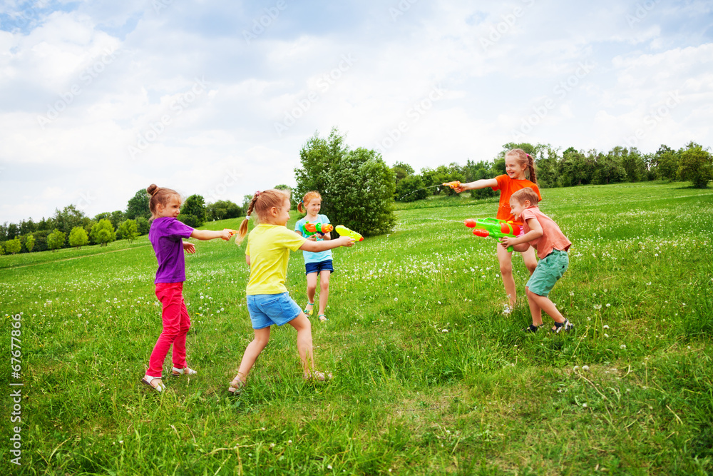 Children play with water guns on a meadow