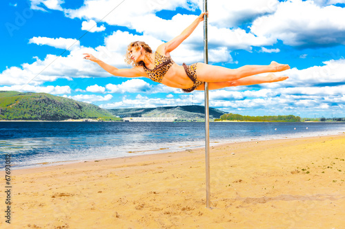 girl make pole dance in a swimsuit on the beach background sky