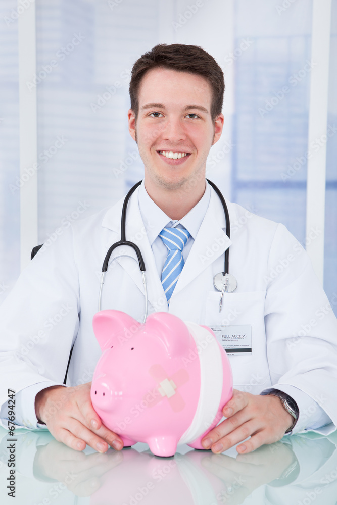 Doctor Holding Piggybank With Bandage In Clinic Doctor Holding Piggybank With Bandage In Clinic