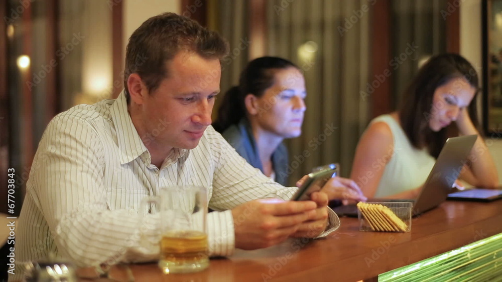 Man using cellphone in pub at night and woman working on technol Man using cellphone in pub at night and woman working on technol