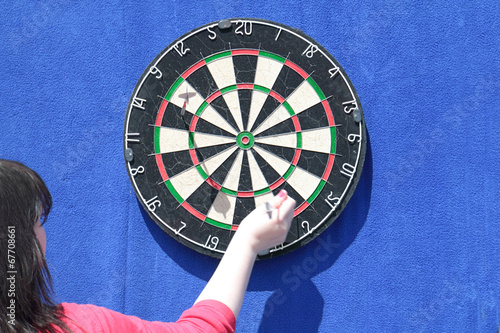 Woman removes darts from dartboard on blue wall at sunny day photo