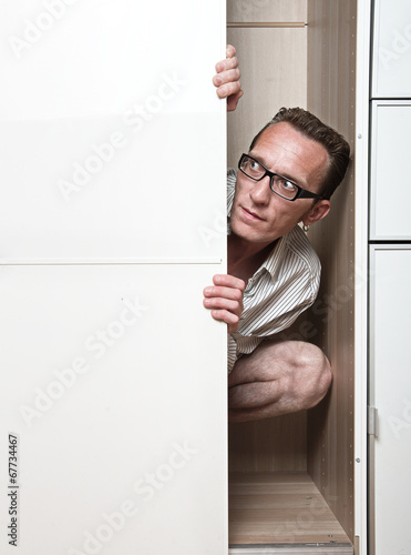 Prying man hiding inside white wardrobe  Copy space left