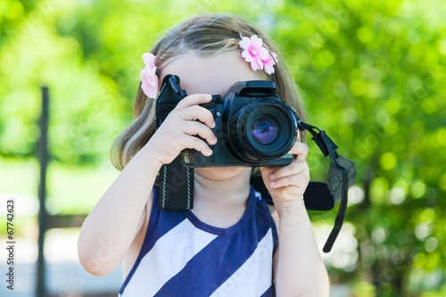 Little girl who takes pictures with a photo camera in park