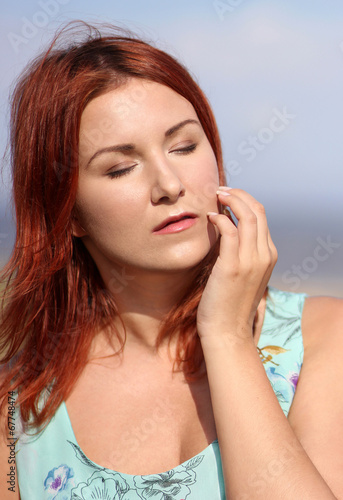 Redhead girl with closed eyes enjoying summer sunlight and wind
