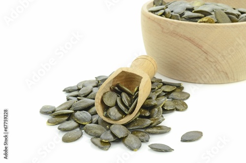 Fotografia A pile of pumpkin seeds with wooden scoop on a white background
