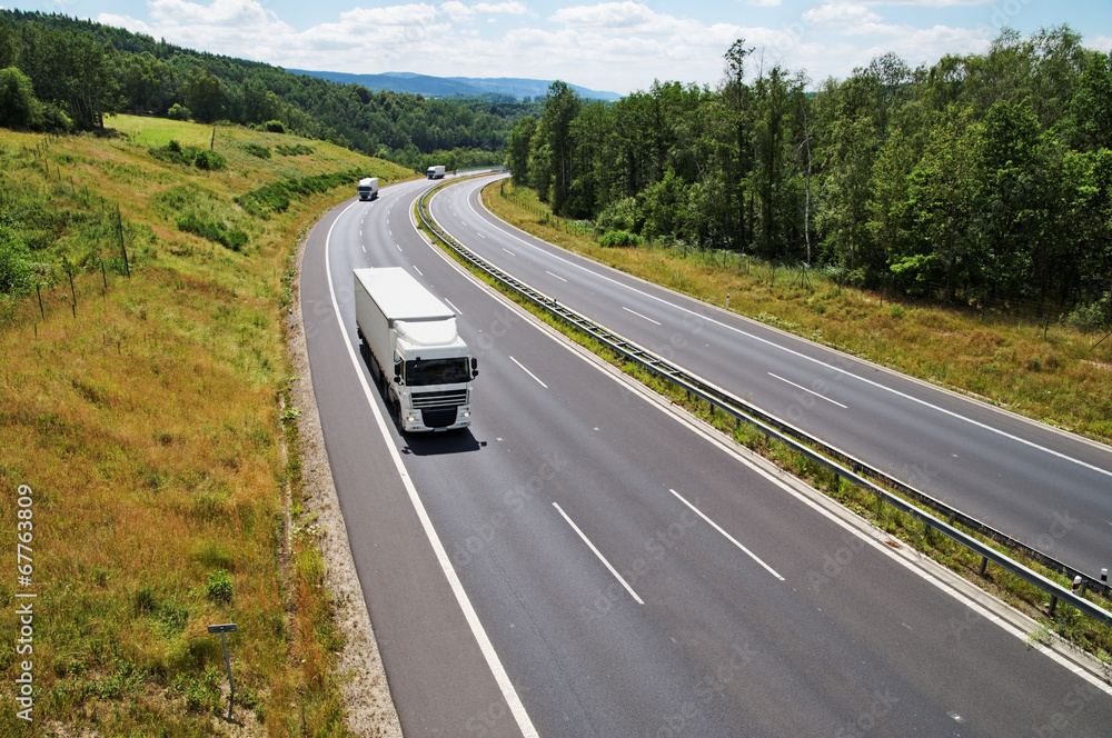 The highway between forests with three oncoming white trucks