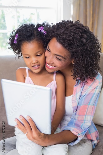 Pretty mother sitting on couch with cute daughter using tablet t