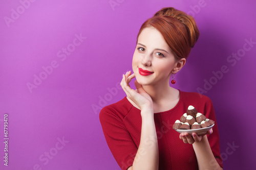 Redhead women with candy on violet background.
