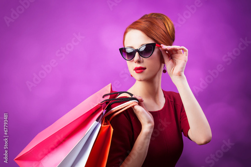 Redhead women with shopping bags on purple background.