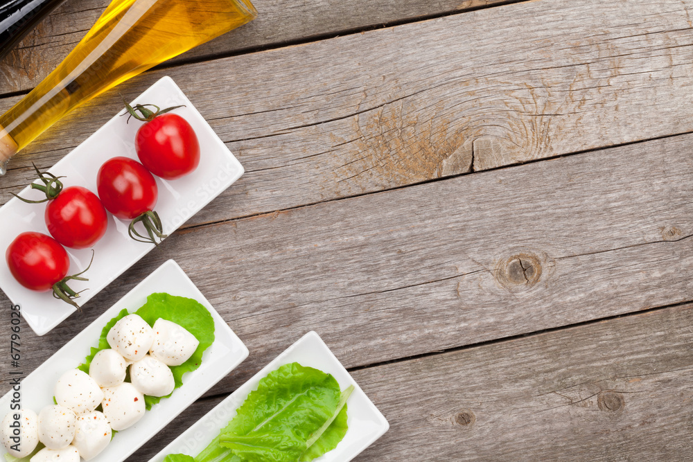 Tomatoes, mozzarella and green salad leaves with condiments Tomatoes, mozzarella and green salad leaves with condiments