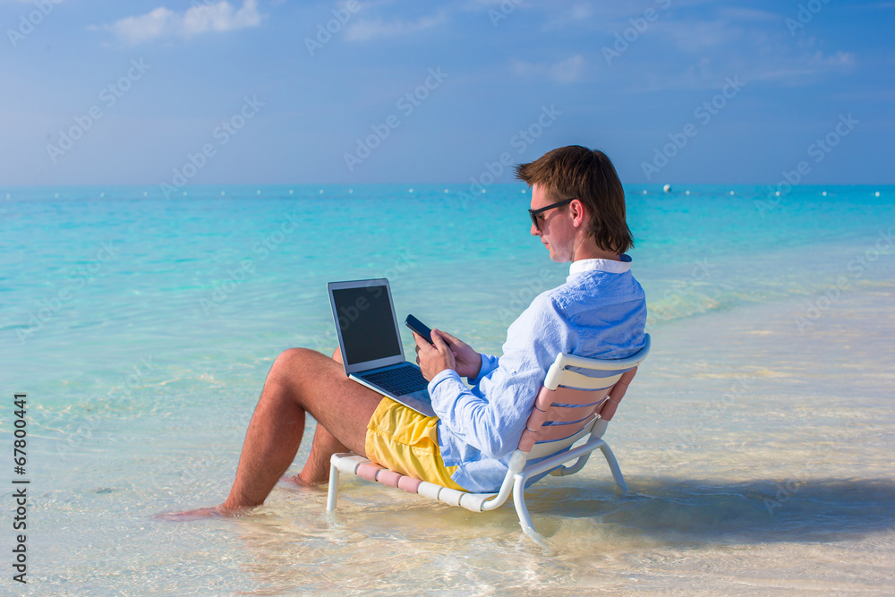 Young man using laptop on tropical beach Young man using laptop on tropical beach
