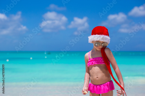 Little cute girl in red hat santa claus on the beach