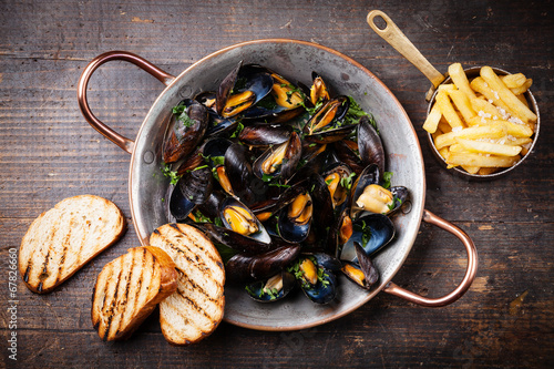 Mussels in copper cooking dish and french fries on dark wooden b