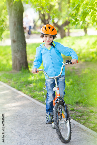 Fototapeta Naklejka Na Ścianę i Meble -  Small boy in blue jacket cycling in a summer park