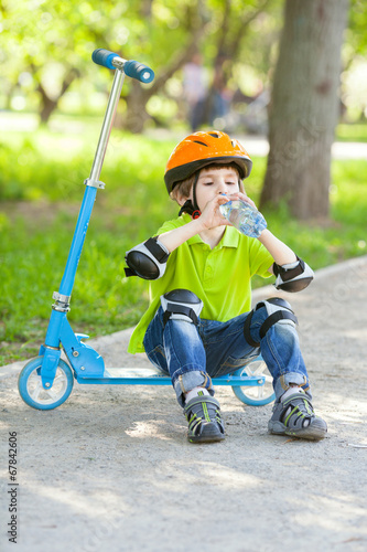 The little boy drinks water from plastic bottle in a city park