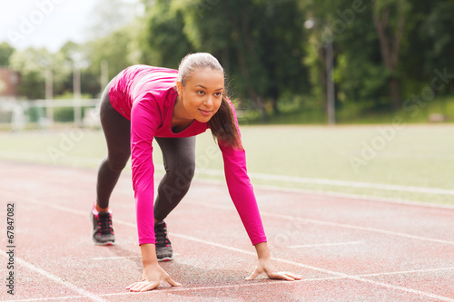smiling young woman running on track outdoors