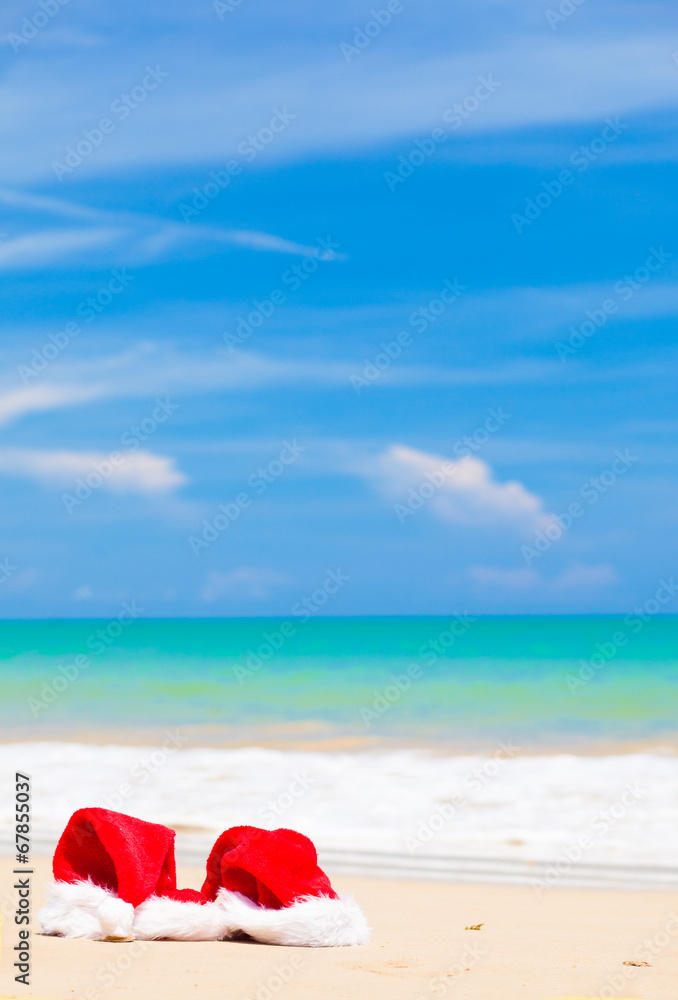 two santa hats lying on tropical sand beach. party. christmas.