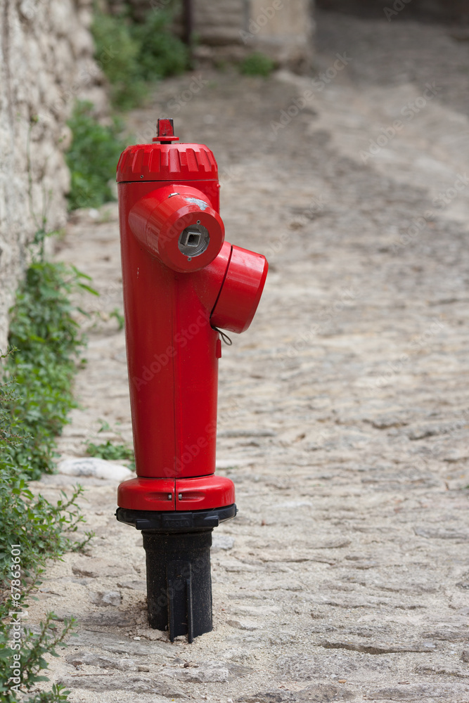 View of a red fire plug located on a street next in an old town View of a red fire plug located on a street next in an old town