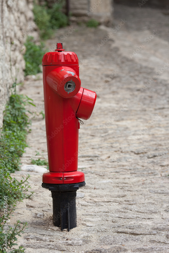 View of a red fire plug located on a street next in an old town