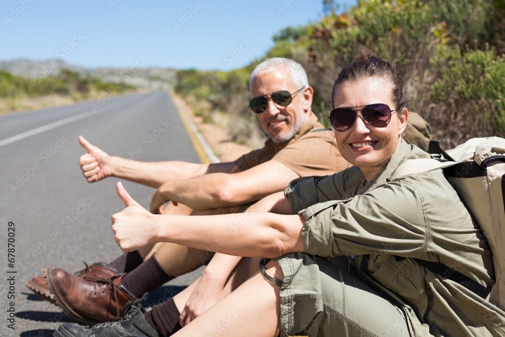 Hitch hiking couple sitting on the side of the road smiling at c
