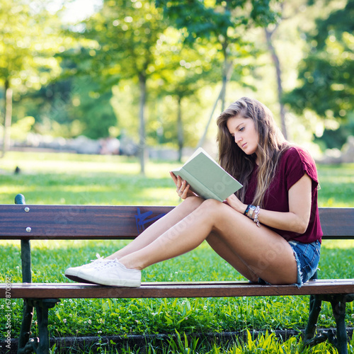 Young woman reading a book under a tree in the park. Filtered im