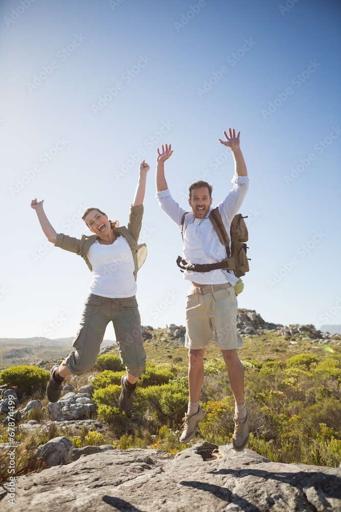 Hiking couple jumping and cheering on rocky terrain Hiking couple jumping and cheering on rocky terrain