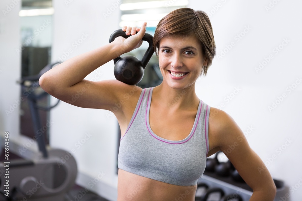 Fit brunette lifting kettlebell smiling at camera Fit brunette lifting kettlebell smiling at camera