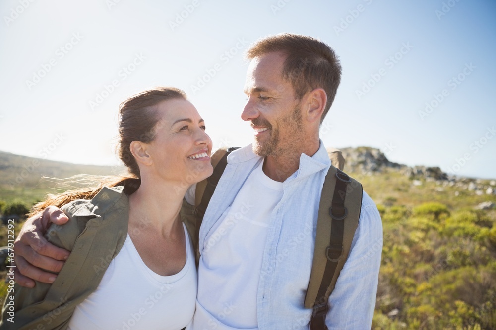 Hiking couple embracing and smiling on country terrain Hiking couple embracing and smiling on country terrain