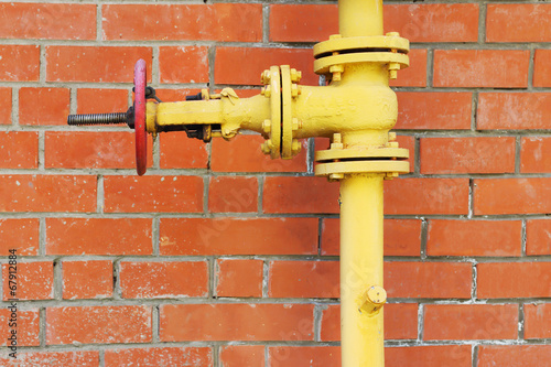 Yellow metal gas pipeline with valve on background of red brick