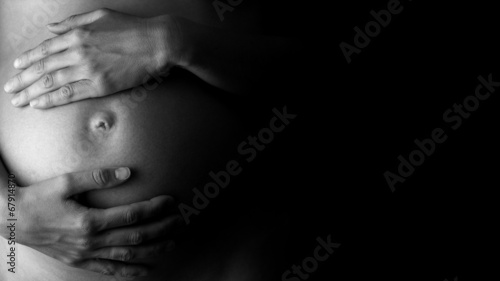Expectant mother holding her belly, in low-key