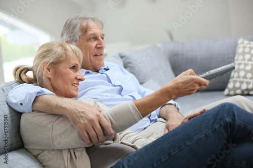 Senior couple sitting in sofa and watching tv © goodluz