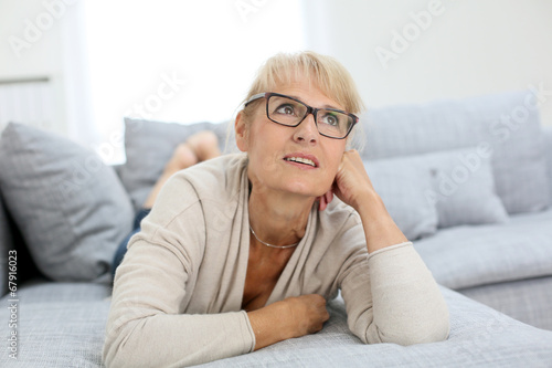 Smiling senior woman with eyeglasses laying on couch