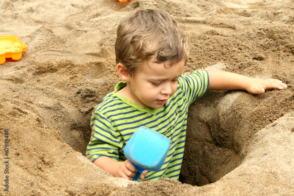 Small boy in a dug out sand hole with shovel Small boy in a dug out sand hole with shovel