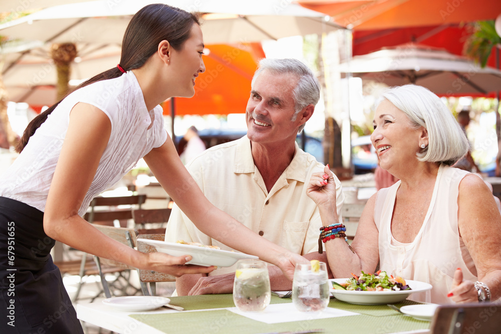 Waitress Serving Senior Couple Lunch In Outdoor Restaurant Waitress Serving Senior Couple Lunch In Outdoor Restaurant
