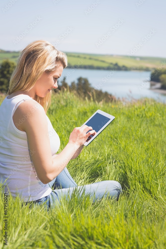 Pretty blonde sitting on grass using her tablet Pretty blonde sitting on grass using her tablet