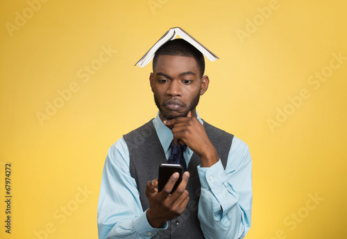 Man holding mobile, book over head isolated on yellow background © pathdoc