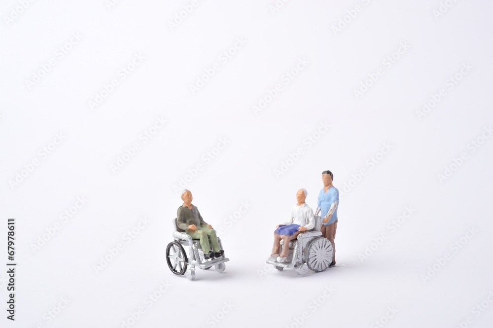 車椅子に乗っている高齢者と介助者のミニチュア人形